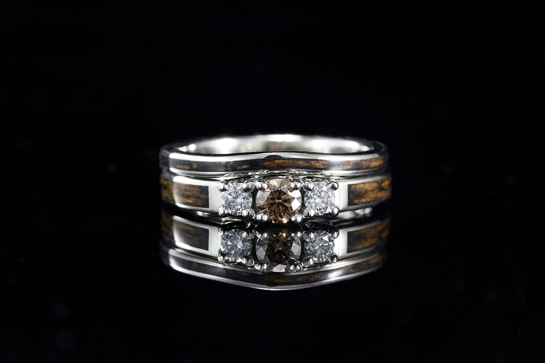 A 3 stone engagement ring with brown wood inlay matching a center brown diamond. Also pictured a matching wedding band in white gold with a brown wood inlay.