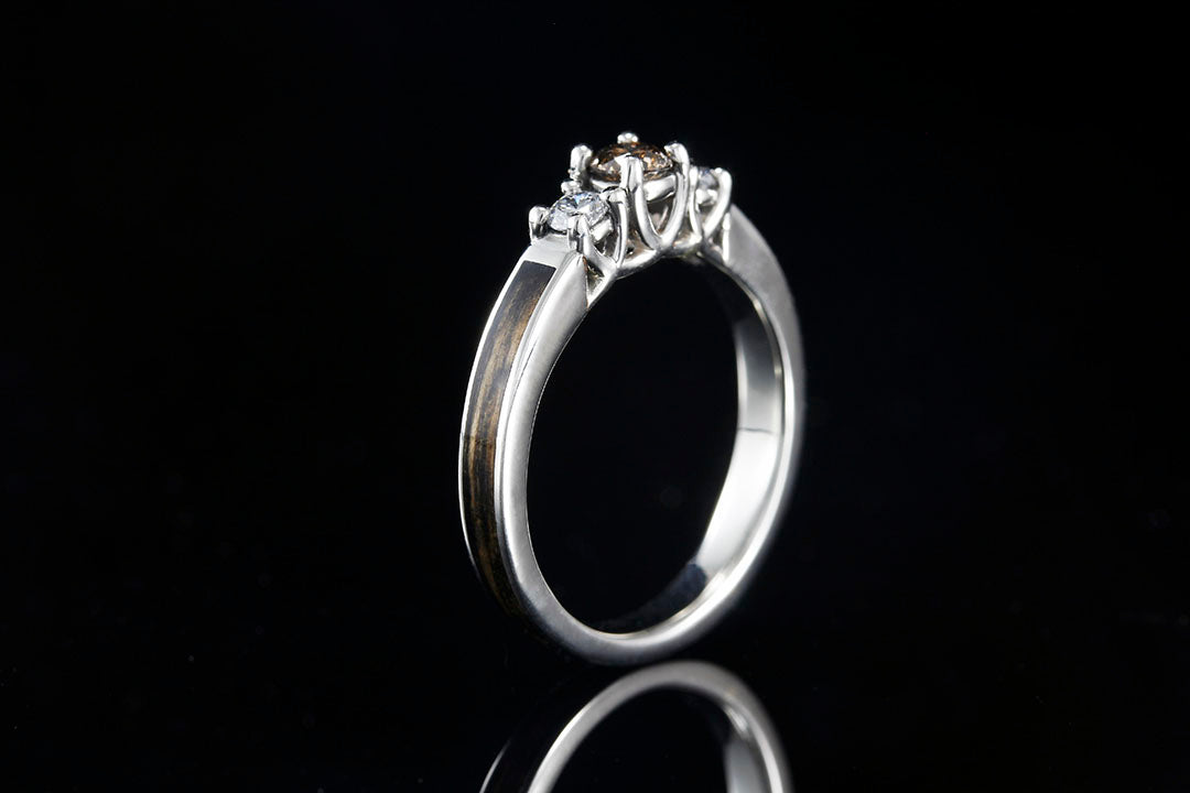 Side profile of wite gold engagement ring with a 3-stone curved prong setting holding 3 diamonds. Center diamond is brown