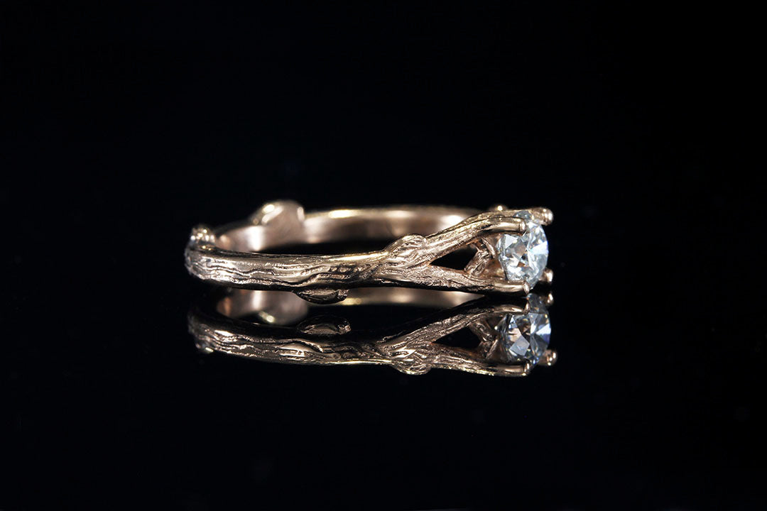 Right side view of a Rose Gold engagement ring holding a clear diamond in its branches 