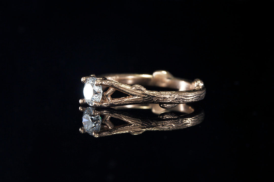 Left side view of a Rose Gold engagement ring holding a clear diamond in its branches 